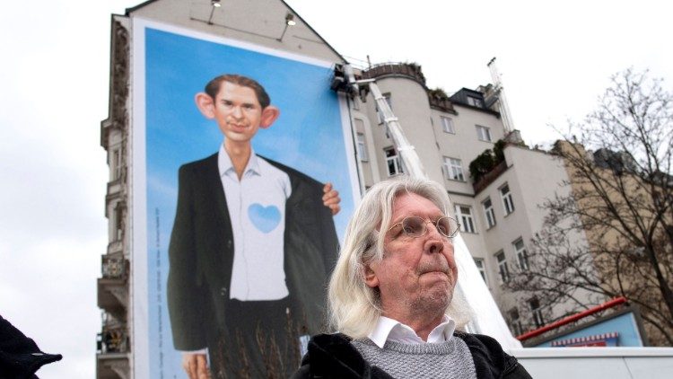 Der Zeichner Gerhard Haderer vor einer Karikatur, die auf die Migrationspolitik von Kanzler Sebastian Kurz zielt