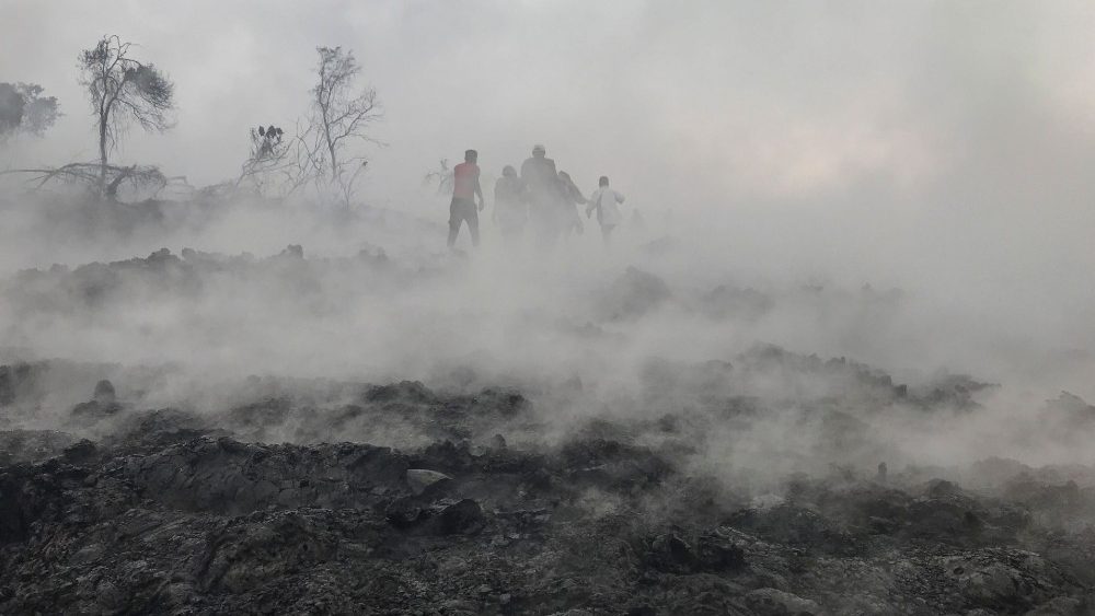 Pessoas são vistas caminhando perto de cinzas fumegantes de manhã cedo em Goma, no leste da República Democrática do Congo, em 23 de maio de 2021, após a erupção do Monte Nyiragongo. (Photo by Moses Sawasawa / AFP)