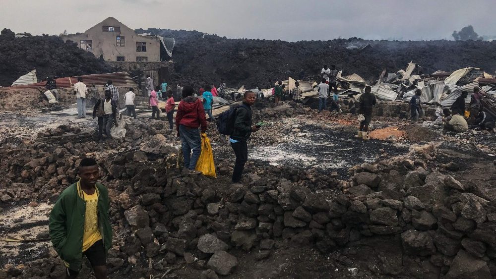 Moradores são vistos próximos a estruturas destruídas perto de cinzas fumegantes de manhã cedo em Goma, no leste da República Democrática do Congo, em 23 de maio de 2021 após a erupção do Monte Nyiragongo.  (Photo by Moses Sawasawa / AFP)