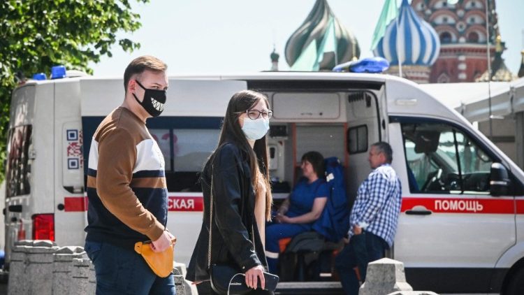 People wearing face masks pass by an ambulance in Red Square in front of St Basil's Cathedral in Moscow