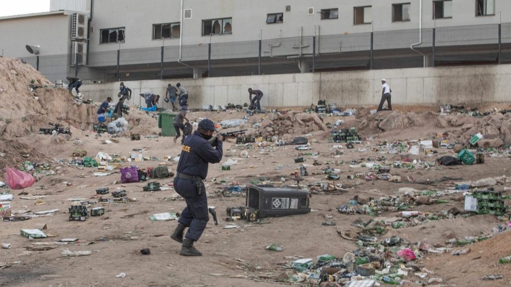 Um membro do SAPS atira balas de borracha para dispersar uma multidão que saqueia do lado de fora de um armazém de armazenamento de álcool em Durban.  (Photo by GUILLEM SARTORIO / AFP)