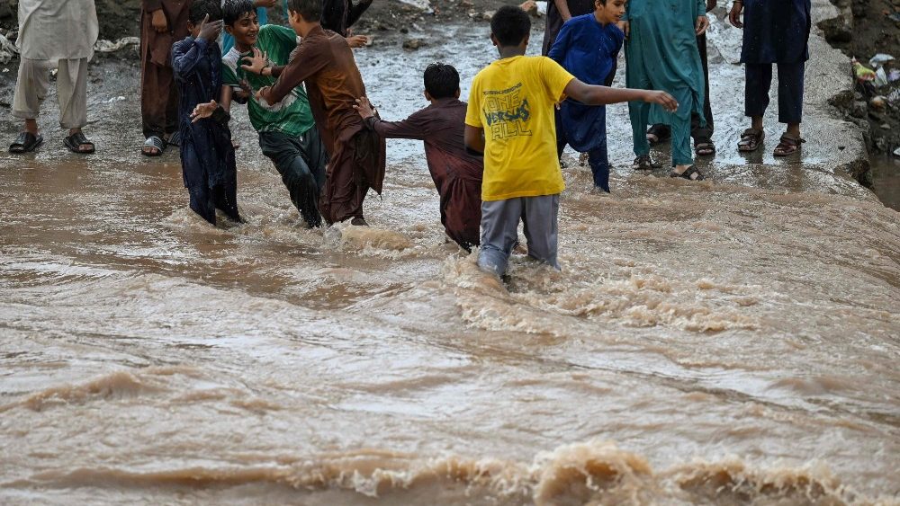Crianças cruzam um riacho em uma estrada que foi inundada após fortes chuvas de monções em Islamabad em 28 de julho de 2021. (Foto de Aamir QURESHI / AFP)
