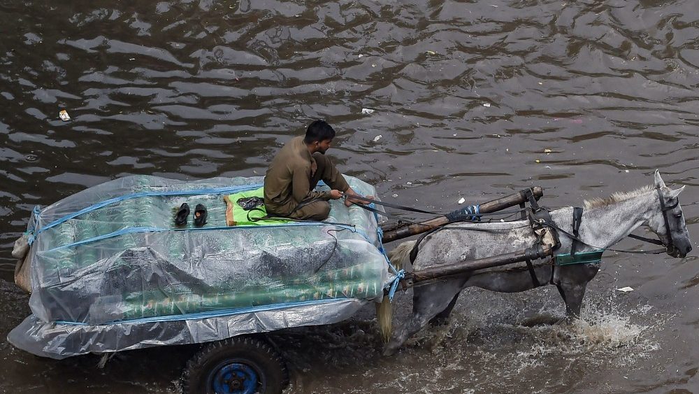 Um homem em uma carroça abre caminho por uma rua inundada após fortes chuvas de monções em Lahore em 31 de julho de 2021. (Foto: Arif ALI / AFP)
