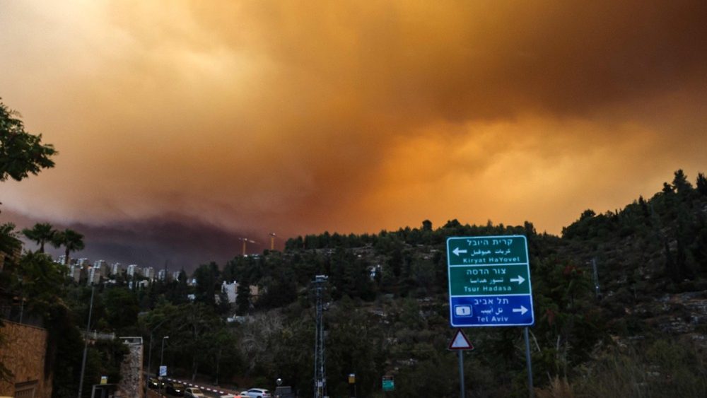 Carros circulam em uma estrada enquanto a fumaça e as chamas sobem de um incêndio florestal nas montanhas de Jerusalém perto de Moshav Shoresh, em 15 de agosto de 2021. . (Photo by MENAHEM KAHANA / AFP)