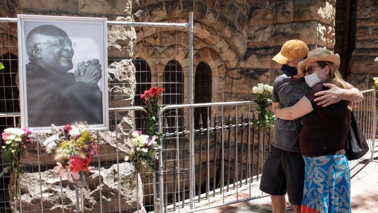 Em frente à Catedral de São Jorge, na Cidade do Cabo, casal olha para foto do arcebispo sul-africano Desmond Tutu.  (Photo by GIANLUIGI GUERCIA / AFP)