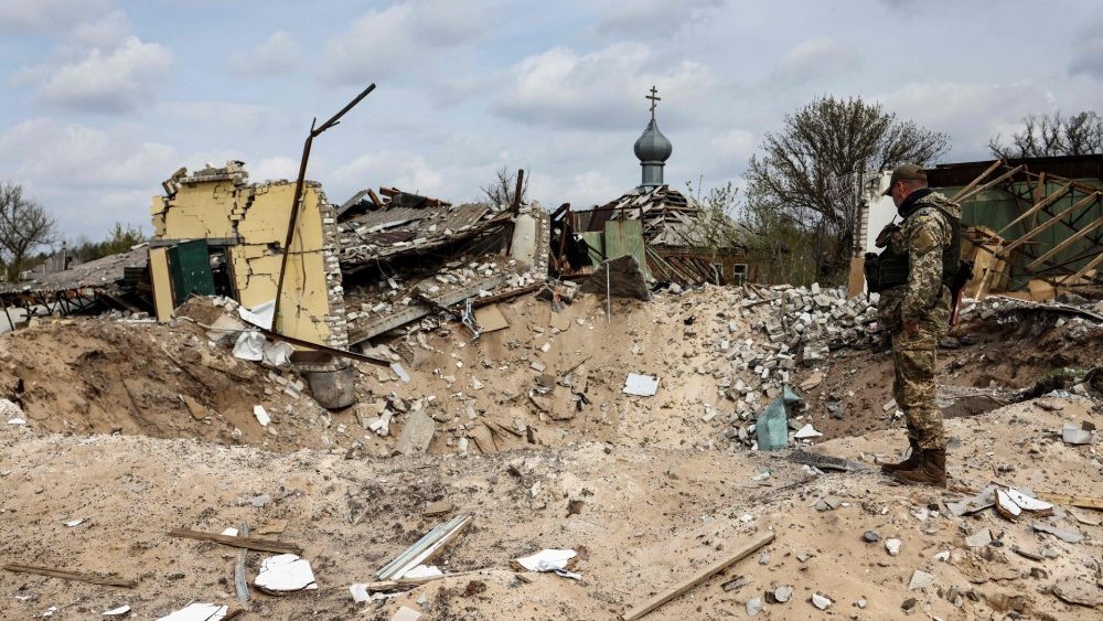 Um soldado ucraniano olha para uma cratera e uma casa destruída é retratada na vila de Yatskivka, leste da Ucrânia, em 16 de abril de 2022. - O foco militar da Rússia agora parece estar em tomar a região leste de Donbas, onde separatistas apoiados pela Rússia controlam Donetsk e áreas de Lugansk. O governador de Lugansk, Serhiy Gaidai, pediu em 16 de abril de 2022 que os civis deixassem a área enquanto ainda podem. (Foto de RONALDO SCHEMIDT/AFP)