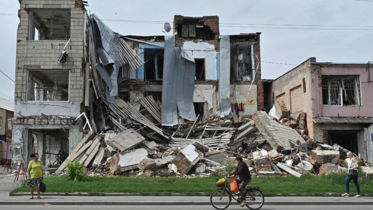 Pedestre e ciclista diante de prédio destruído por foguetes russos em Okhtyra, região de Summy., em 2 de agosto de 2022. (Photo by Genya Savilov/AFP)