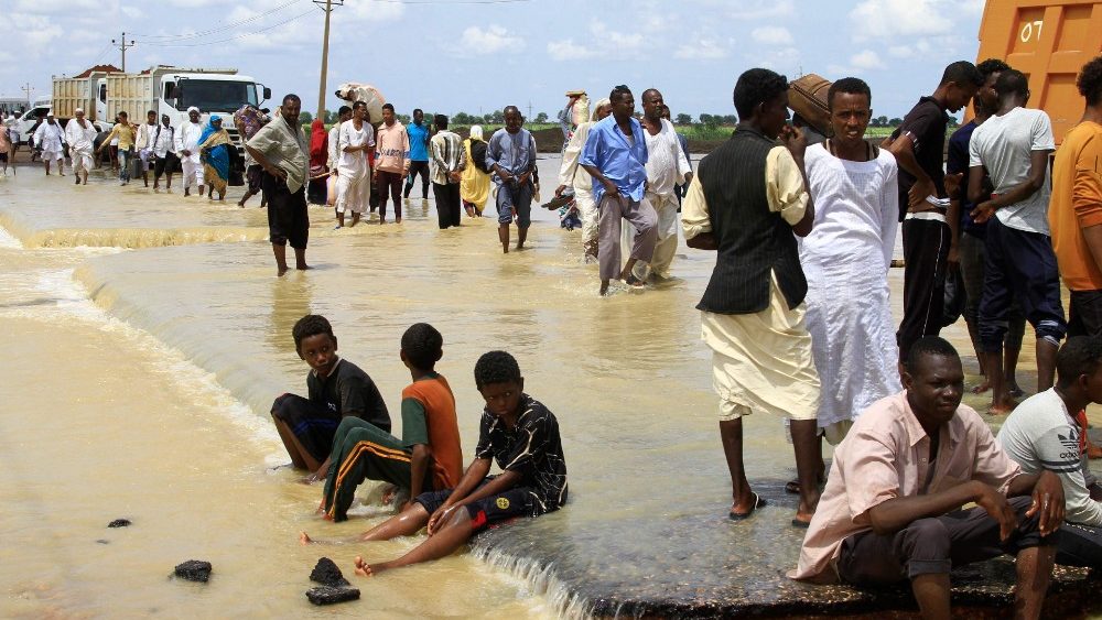 Sudaneses atravessam uma estrada inundada na cidade de Iboud, 250 km ao sul da capital Cartum, em 22 de agosto de 2022. (Foto de Ebrahim Hamid/AFP)