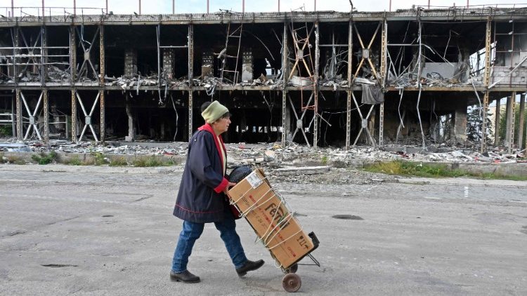 Uma moradora local carrega seu carrinho por um prédio destruído em Izyum, região de Kharkiv, em 28 de setembro de 2022, em meio à invasão russa da Ucrânia. (Foto de SERGEY BOBOK/AFP)