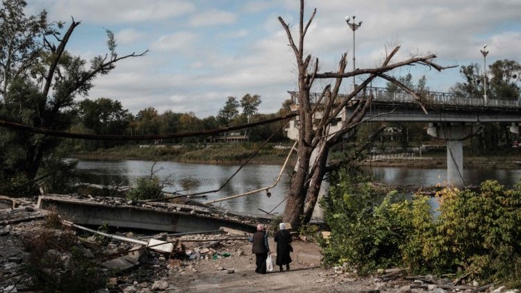 Duas mulheres caminham até um ponto de espera por um barco para cruzar o rio Siverskyi Donets ao lado de uma ponte destruída na cidade recentemente retomada de Sviatohirsk, na região de Donetsk, em 9 de outubro de 2022, em meio à invasão russa da Ucrânia. (Foto de Yasuyoshi CHIBA/AFP)