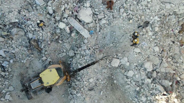 Uma vista aérea mostra membros da defesa civil síria, conhecidos como Capacetes Brancos, observando enquanto uma escavadeira trabalha nos escombros de um prédio desabado na vila de Salqin, na fronteira com a Turquia, em 10 de fevereiro de 2023, quatro dias após um terremoto na Turquia e na Síria que matou 21.000 pessoas. (Foto de Mohammed AL-RIFAI / AFP)