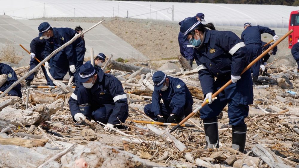 Membros da brigada de incêndio local procuram os restos mortais de pessoas desaparecidas em uma praia em Namie, Prefeitura de Fukushima, norte do Japão, 11 de março de 2021. 