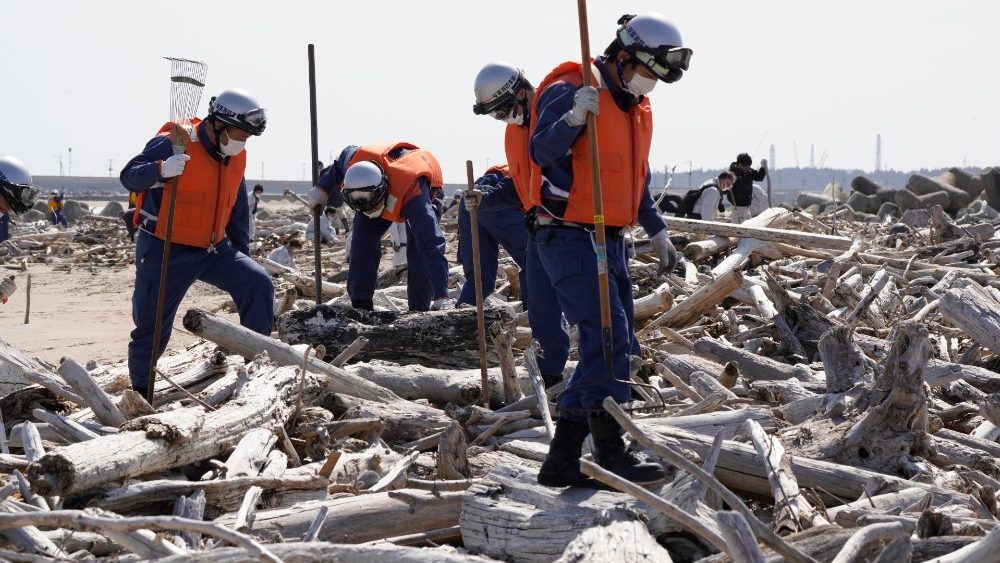 Membros da brigada de incêndio local procuram os restos mortais de pessoas desaparecidas em uma praia em Namie, Prefeitura de Fukushima, norte do Japão, 11 de março de 2021.