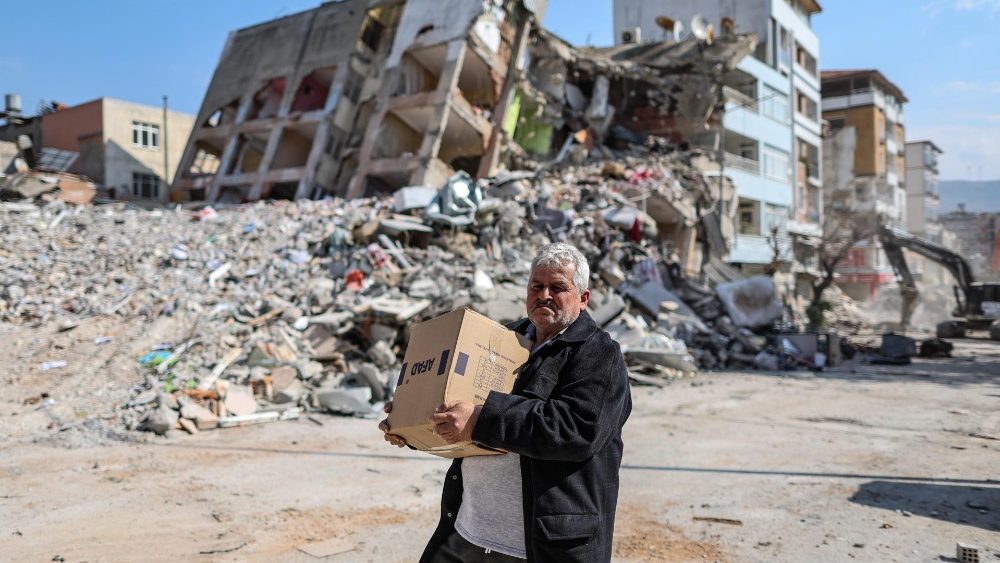 Um homem carrega uma caixa de ajuda passando por edifícios desmoronados após fortes terremotos no distrito de Samandag de Hatay, Turquia, 23 de fevereiro de 2023.  EPA/ERDEM SAHIN