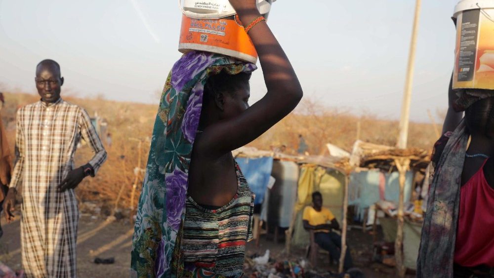 Pessoas que fugiram da violência no Sudão carregam recipientes de plástico em suas cabeças enquanto passam pelo assentamento informal que cresce perto da área de trânsito de refugiados e repatriados estabelecida pelo ACNUR na cidade de Renk, no estado do Alto Nilo, Sudão do Sul, 11 de maio de 2023. EPA /AMEL DOR