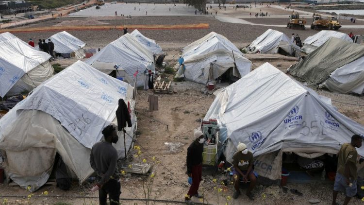 Migrants and refugees stand next to tents in the Mavrovouni camp on the island of Lesbos, Greece