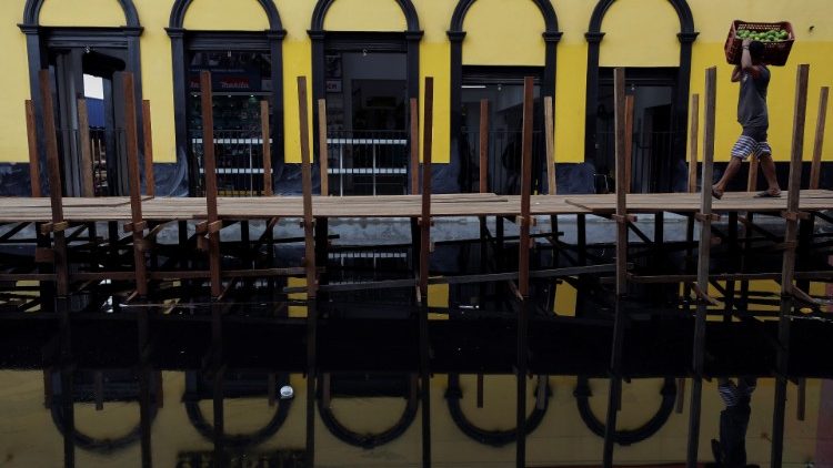 Homem carrega caixa com laranjas enquanto caminha sobre passarela de madeira instalada pela prefeitura em uma rua inundada pelas águas do rio Negro no centro de Manaus, no Estado do Amazonas, Brasil 17 de maio de 2021. REUTERS / Bruno Kelly