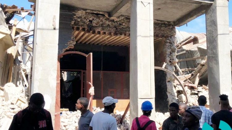 People stand in front of collapsed buildings following an earthquake in Jeremie