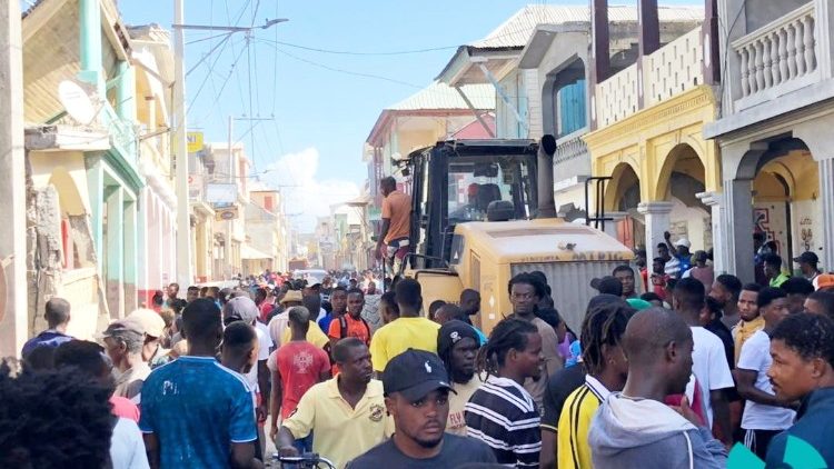 People walk along the street next to destroyed buildings following an earthquake in Jeremie