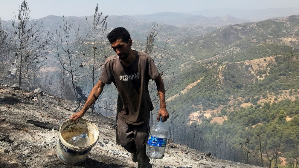 A man carries water containers as he works with others to douse hotspots in an area hit by a wildfire in El Bir village, Algeria