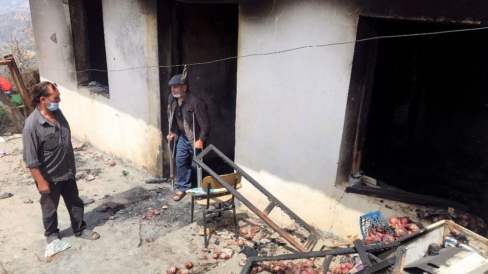 Lyazid Tazibt stands with his brother Khelaf at their home that was burnt following a wildfire in the village of Ait Sid Ali