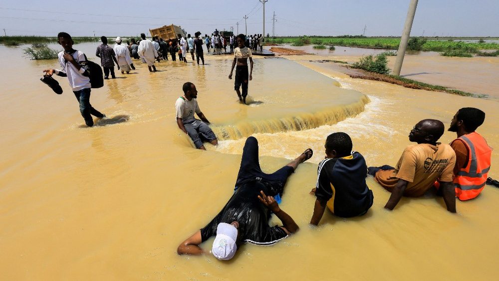 Pessoas descansam enquanto outras cruzam a água durante enchentes na localidade de Al-Managil, no estado de Jazeera, Sudão, 23 de agosto de 2022. REUTERS/Mohamed Nureldin Abdallah
