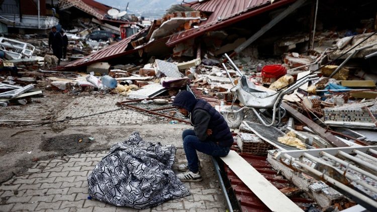 Mężczyzna siedzący obok ciała zawiniętego w koc po trzęsieniu ziemi, Hatay, Turcja, 7 lutego 2023
