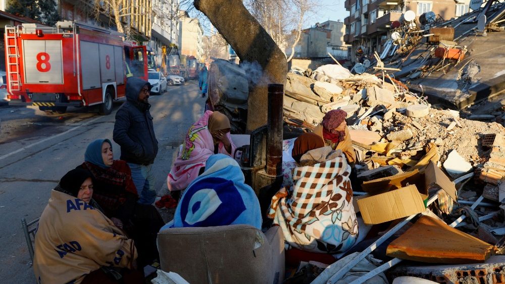 Pessoas sentam-se ao lado de escombros no local de um prédio que desabou após um terremoto em Kahramanmaras, Turquia, 8 de fevereiro de 2023. REUTERS/Suhaib Salem