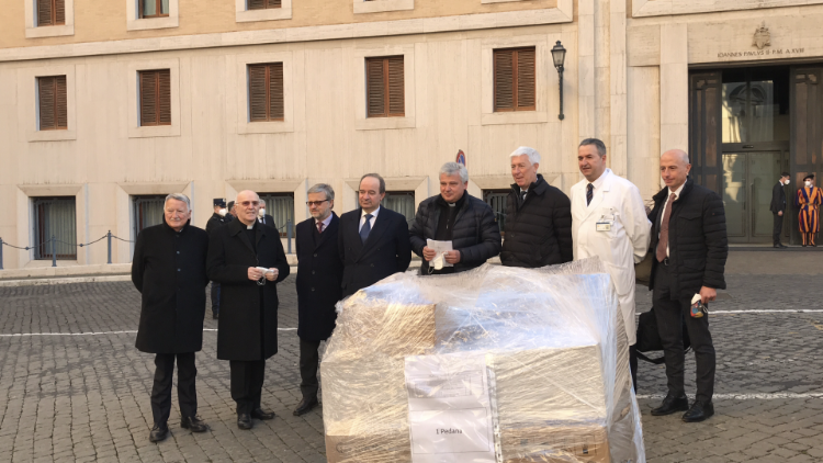 Foto di gruppo con uno dei bancali con i farmaci e i dispositivi medici essenziali. Sullo sfondo, l'ingresso di Casa Santa Marta